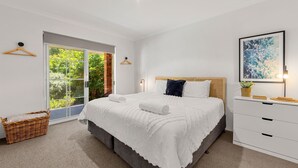 A modern bedroom with a large bed, a wooden headboard, a white dresser, and a framed artwork on the wall. - Callala Bay n Beach House - Pet Friendly with Fireplace (Callala Bay)