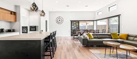 Uma cozinha moderna com ilha central, área de refeições com sofá e cadeiras, e uma janela ampla que proporciona iluminação natural.