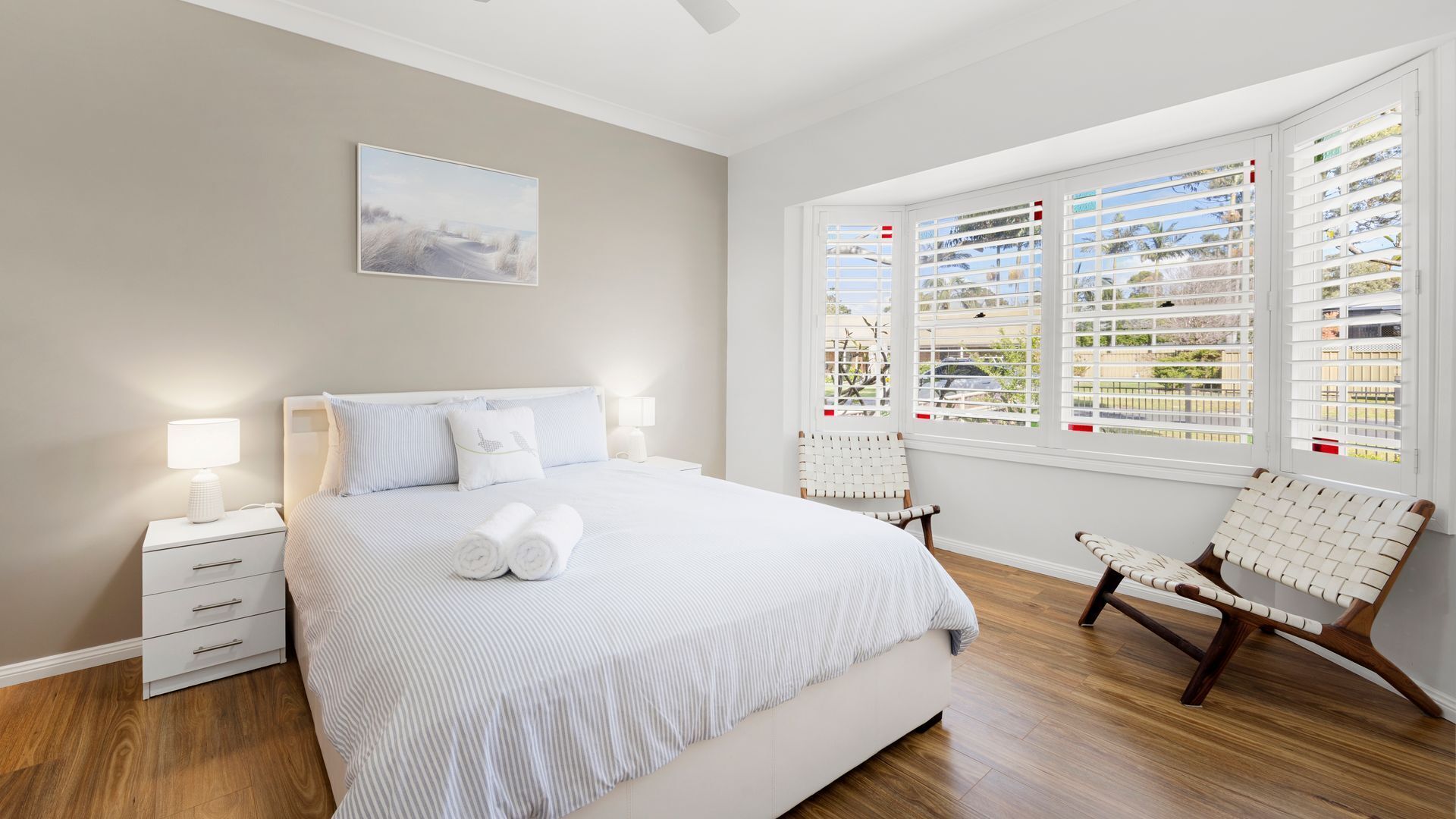 A bedroom with a large bed, a bedside table with a lamp, a chair, and a window with blinds.