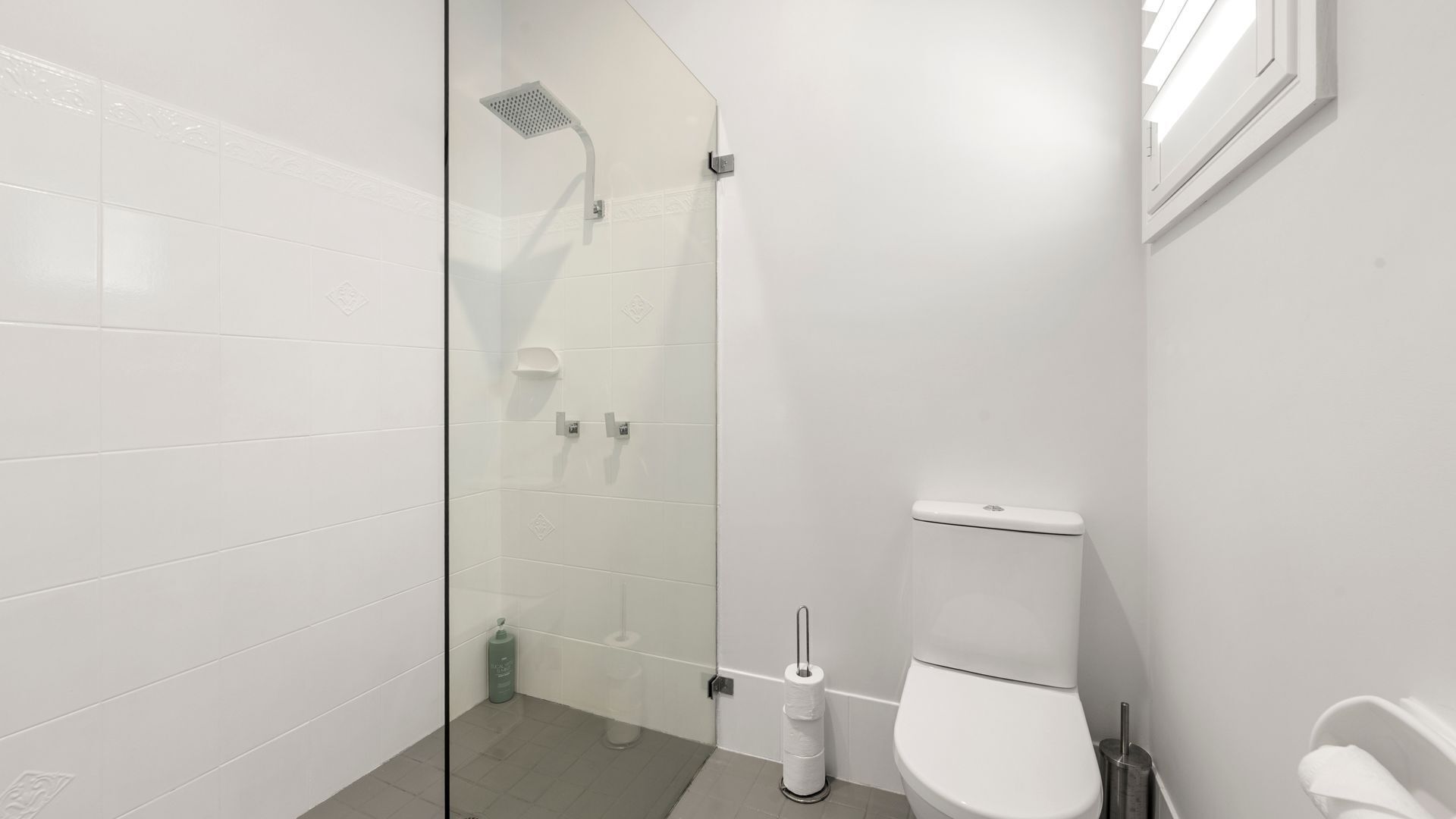 Un baño moderno con azulejos blancos, cabina de ducha de vidrio, inodoro y secador de manos.