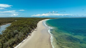 A beach with clear turquoise waters and a sandy shore, surrounded by dense green vegetation. - Dolphin Cove - Pet Friendly with Fireplace (Callala Bay)