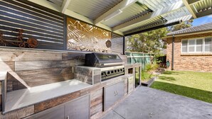 Area cucina esterna con barbecue integrato, spazio per il vino e una parete decorativa.