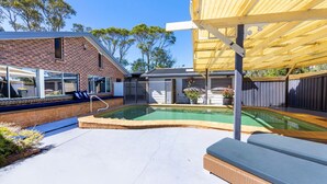 En baghave med swimmingpool, overdækket terrasse og et murstenshus.
