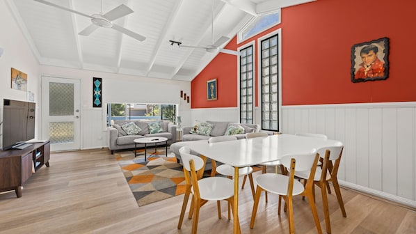 A spacious living room with a large white table and chairs, a grey sofa, and a red accent wall.