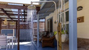 A covered outdoor area with a showerhead, wicker furniture, and a wooden pergola.