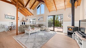 Un salón espacioso con techo alto, chimenea y un amplio ventanal corredero que da a una terraza exterior.