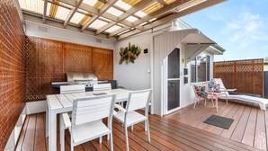 An outdoor patio with a grill, white chairs, and a wooden deck. - Osprey - Pet Friendly Waterfront (Callala Bay)