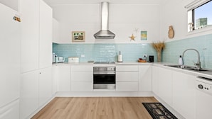 A modern kitchen with white cabinets, a stainless steel range hood, a built-in oven, and a window with a view of the city. - Osprey - Pet Friendly Waterfront (Callala Bay)