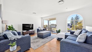 A modern living room with a flat-screen TV, two sofas, a coffee table, and a large window offering a view of the outdoors. - Sandy Adventures - Pet Friendly - 1 Min to Beach (Callala Beach)