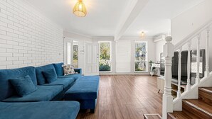 Un salón espacioso con un sofá seccional azul, una escalera con balaustres blancos y un televisor de pantalla plana grande.