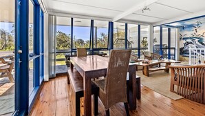 Un amplio comedor al aire libre con mesa y sillas de madera, ventanas grandes y vistas del paisaje circundante.