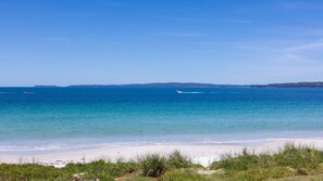 A beach with clear blue water, a sandy shore, and distant hills. - Zara del Mar - Pet Friendly Absolute Waterfront (Callala Beach)