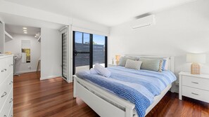 Een slaapkamer met een groot bed, een nachtkastje, een kaptafel, een dressoir, een spiegel en een glazen schuifdeur die leidt naar een balkon.
