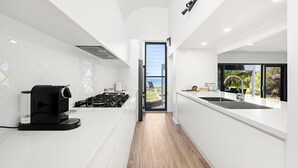Una cocina moderna con estufa a gas, cafetera y vistas al exterior a través de un amplio ventanal corredero.