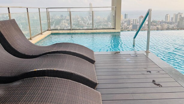 Una piscina infinita en la azotea con vistas a la ciudad, una terraza de madera y sillones de descanso.