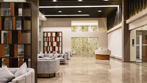 Un hall espacioso con mostrador de recepción, zona de estar con sofás y una pared decorativa con diseño geométrico.