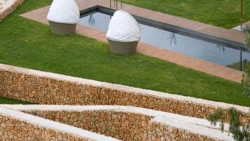 Una piscina con dos grandes fuentes de agua blancas, un muro de contención de piedra y una zona ajardinada.