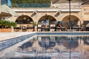 A swimming pool with lounge chairs and umbrellas, a stone archway, and a view of the sky. - Hotel Hospes Maricel & Spa (Ca's Catala)