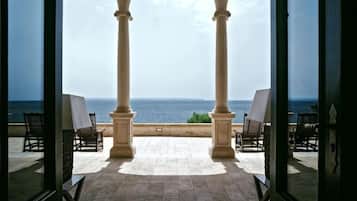 Vista a través de un ventanal hacia una terraza con mesa de billar, dos sillas y vista al mar.