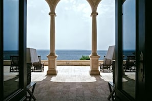 A view through a glass door to a terrace with a pool table, two chairs, and a view of the sea.