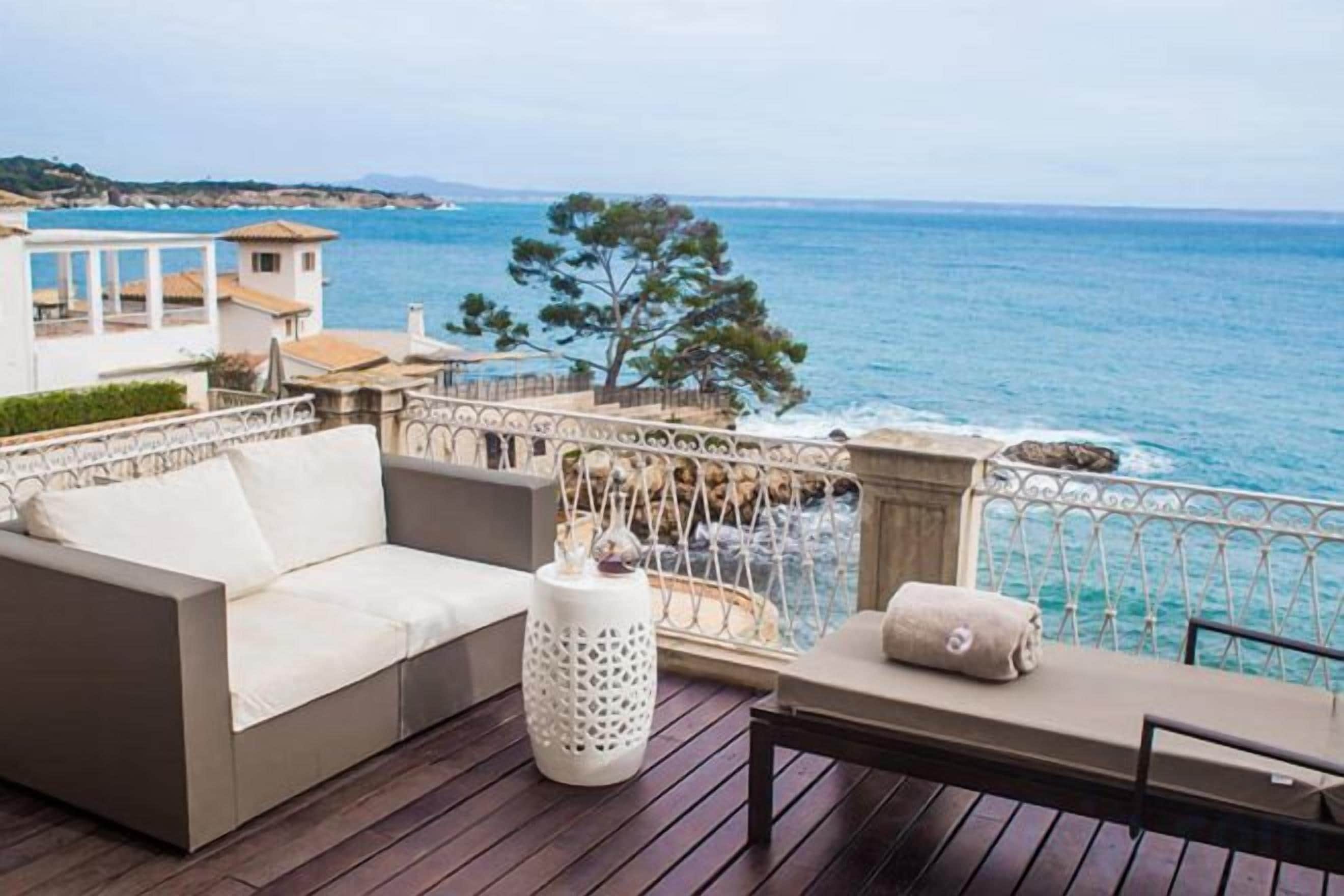 Una terraza con sofá, una mesa y barandilla con vista al mar.