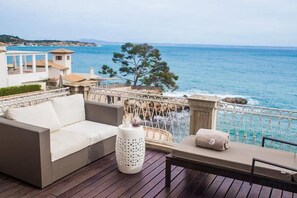 A deck with a sofa, a table, and a railing overlooking the sea. - Hotel Hospes Maricel & Spa (Ca's Catala)