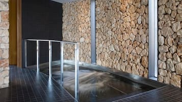 Un espacio de spa con pared de piedra, barandilla metálica y suelo de baldosas negras.