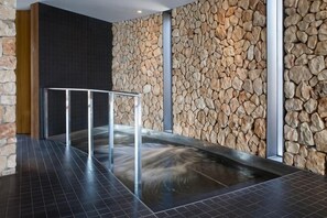 A spa area with a stone wall, a metal railing, and a black tiled floor.