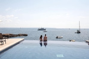 Um casal em uma piscina infinita com vista para o mar e barcos.