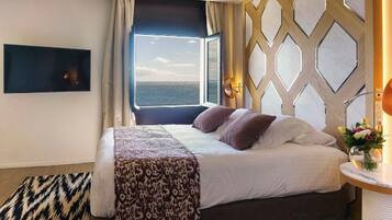 Habitación de hotel con cama, vista al mar, televisor montado en la pared y alfombra estampada.