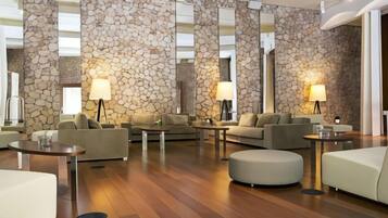 Un vestíbulo de hotel moderno con paredes de piedra, varias zonas de estar e iluminación ambiental.