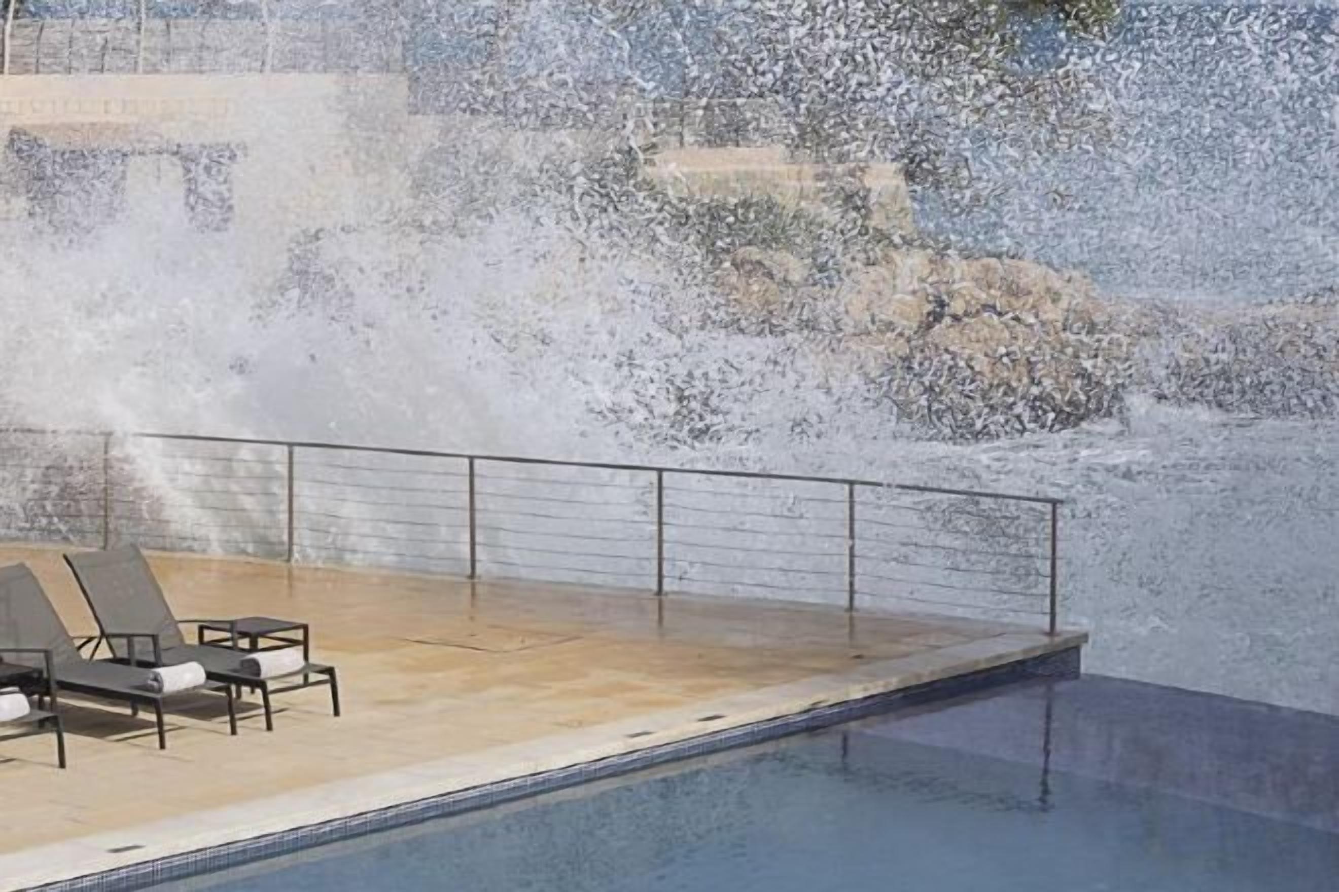 Un área de piscina con fuente de agua, sillas de descanso y barandilla.