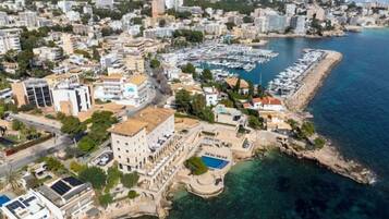 Vista aérea de un pueblo costero con edificios, un puerto deportivo y aguas azules cristalinas.