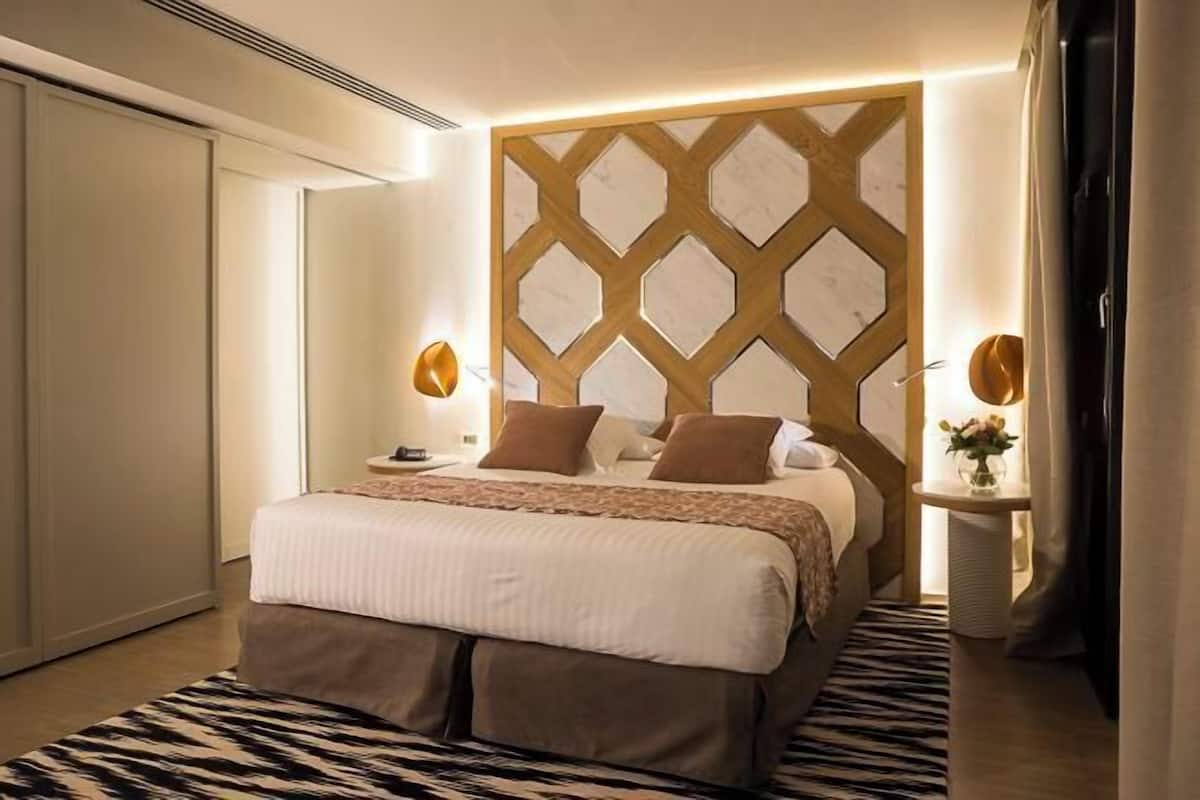 Hotellihuone, jossa on sänky, yöpöydät, geometrisesti kuvioitu seinä ja kuvioitu matto.