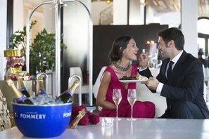 A dining table with a blue bowl labeled 'POMMERY' containing champagne bottles, a plate of food, and a waiter serving a meal. - Hotel Hospes Maricel & Spa (Ca's Catala)