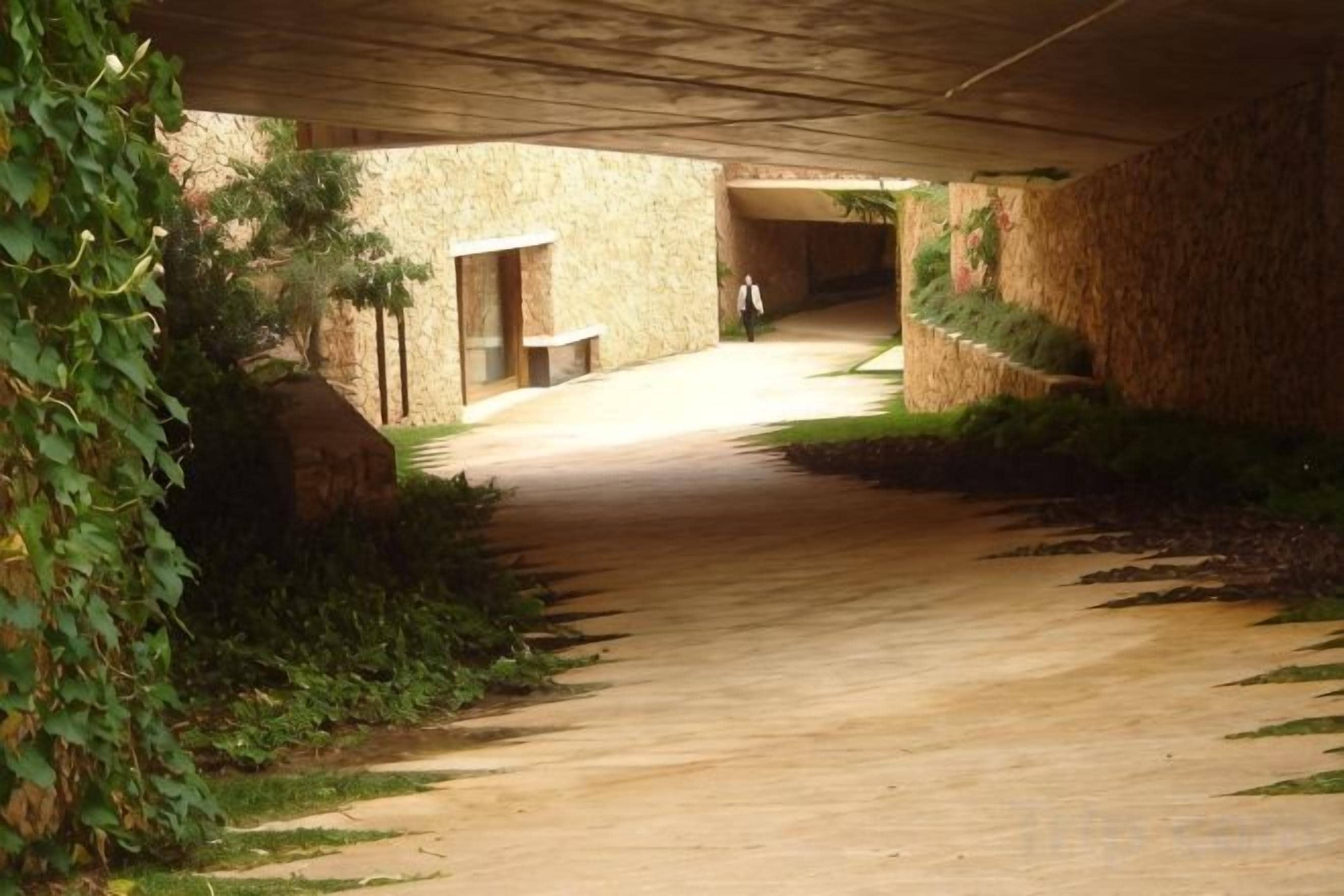 Un pasillo interior con piso de concreto, paredes de piedra y una persona caminando.