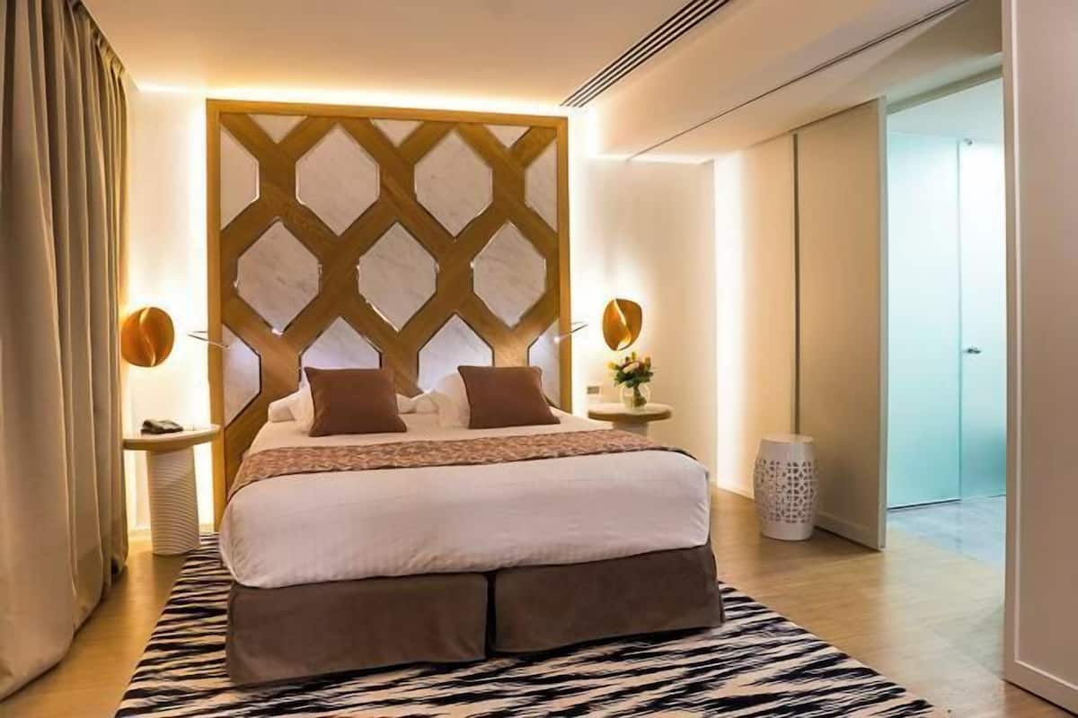Hotellihuone, jossa on sänky, koristeellinen seinä, yöpöytälamput ja yöpöytä.