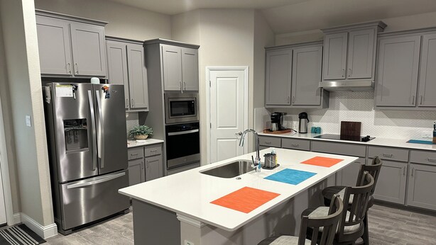 A modern kitchen with grey cabinets, stainless steel appliances, and a central island with orange and blue placemats.