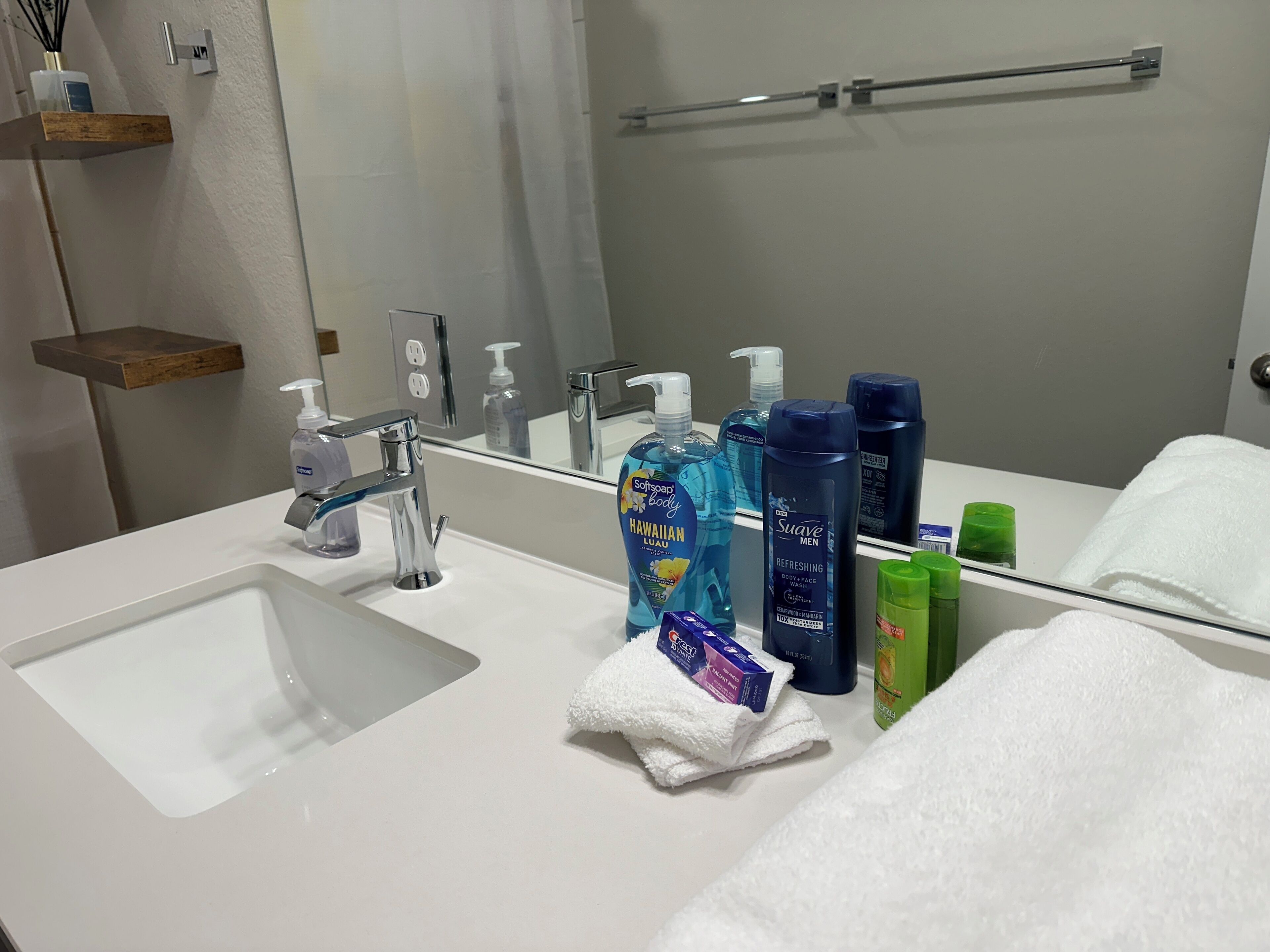 Ein Badezimmer mit einem weißen Waschbecken, einem Spiegel und Pflegeprodukten wie Duschgel, Shampoo und Conditioner.