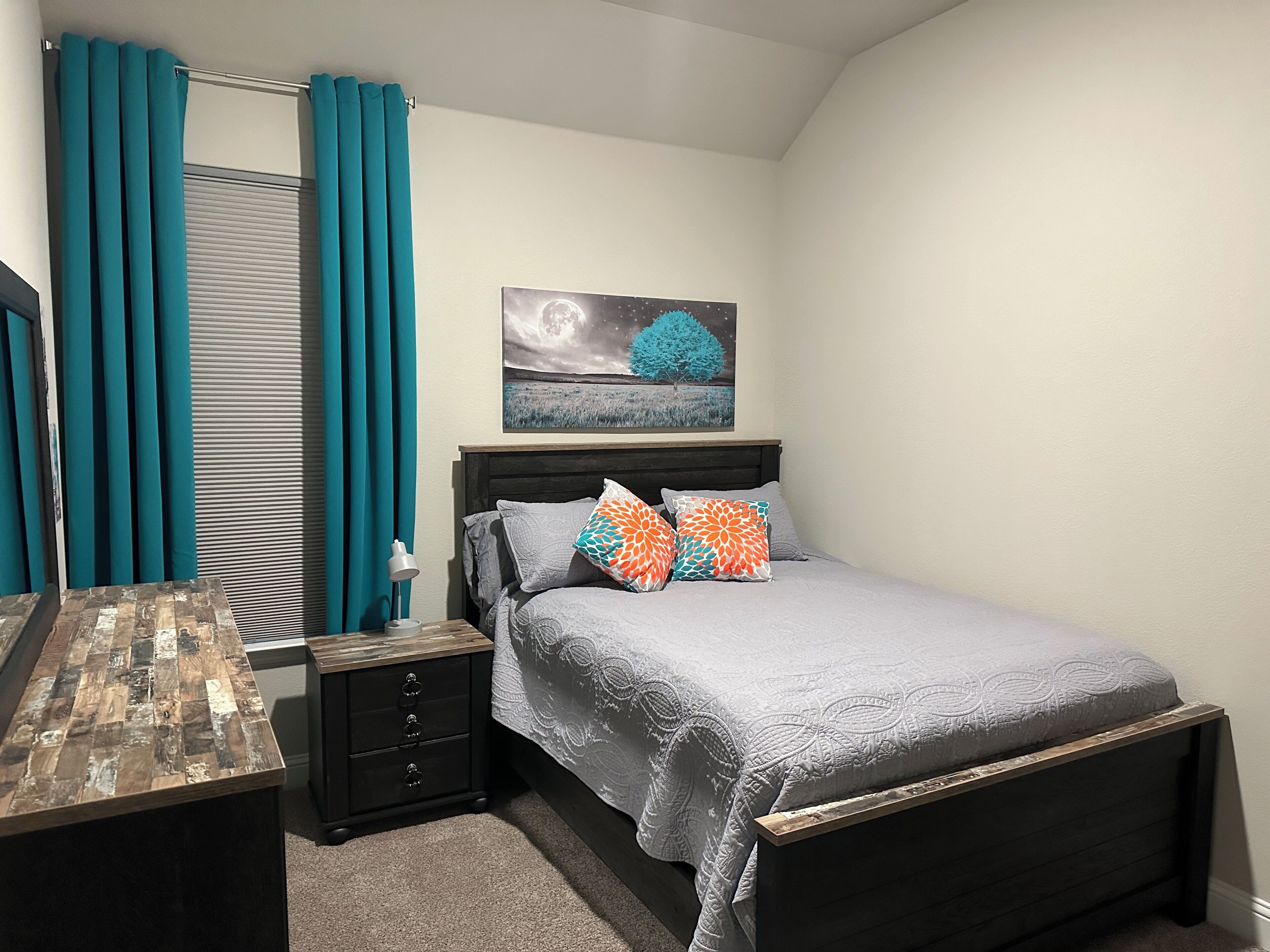 A bedroom with a bed, a nightstand, a dresser, and a painting on the wall.