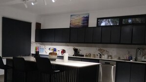 A modern kitchen with dark cabinetry, a central island with seating, a stainless steel dishwasher, and a black countertop. - Villa atomium ile maurice souillac 127m2 100m to the beach (Souillac)