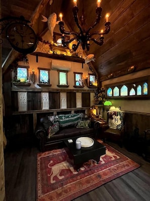 A cozy room with a wooden ceiling, a chandelier, a clock, and a fireplace with stained glass windows.