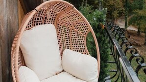 Una sedia in vimini con cuscini su un balcone vista alberi.