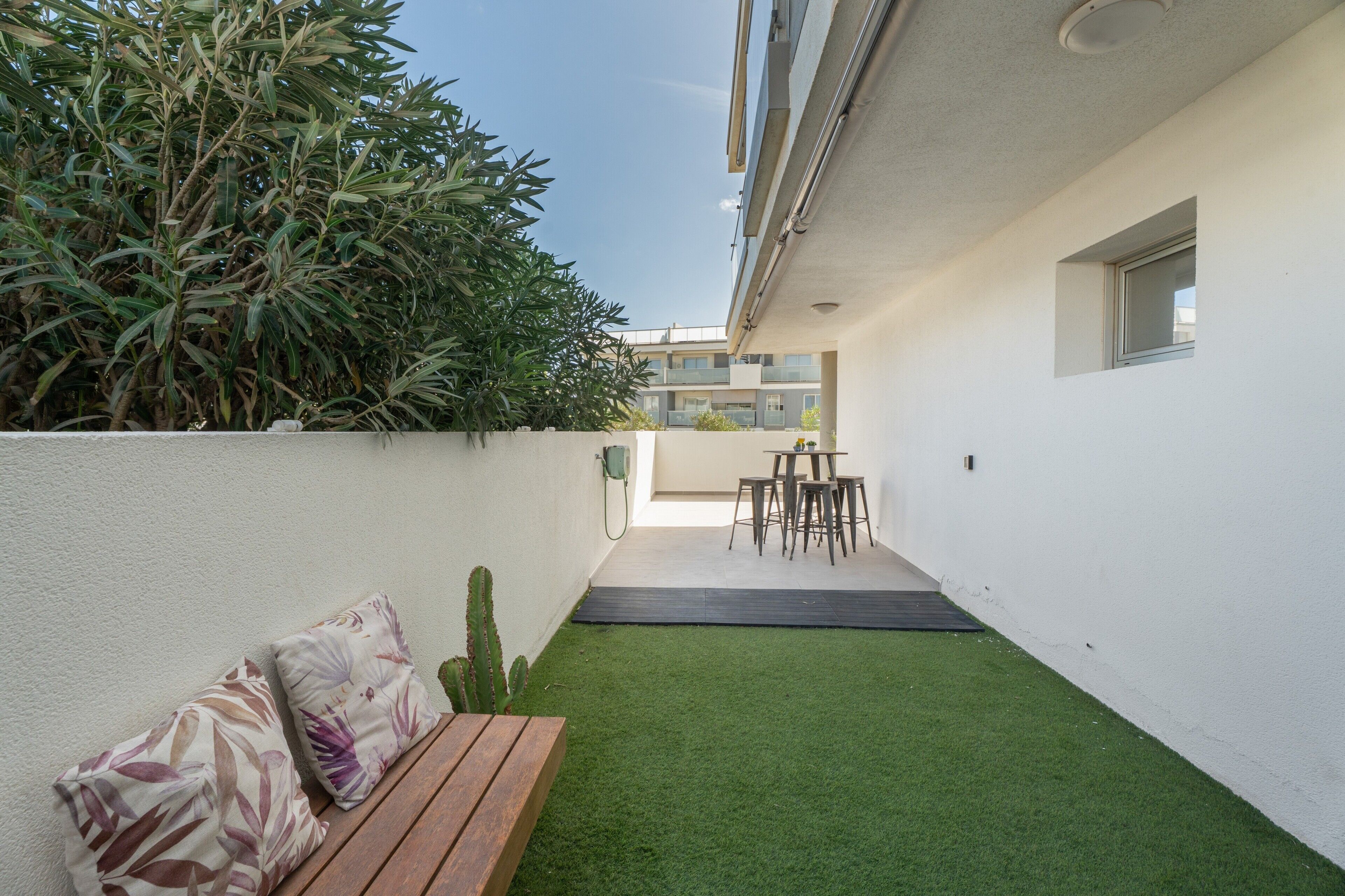 A modern outdoor patio with a wooden bench, a small table, and chairs.