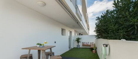 A patio with a table and stools, a small garden area with a potted plant, and a green wall-mounted device.