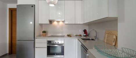 Una cocina moderna con un refrigerador de acero inoxidable, horno empotrado y una lámpara colgante.