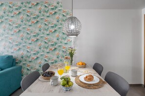 Une table à manger agrémentée d’un papier peint aux motifs tropicaux, d’un luminaire suspendu en fibres tressées et d’une mise en place pour le petit-déjeuner.