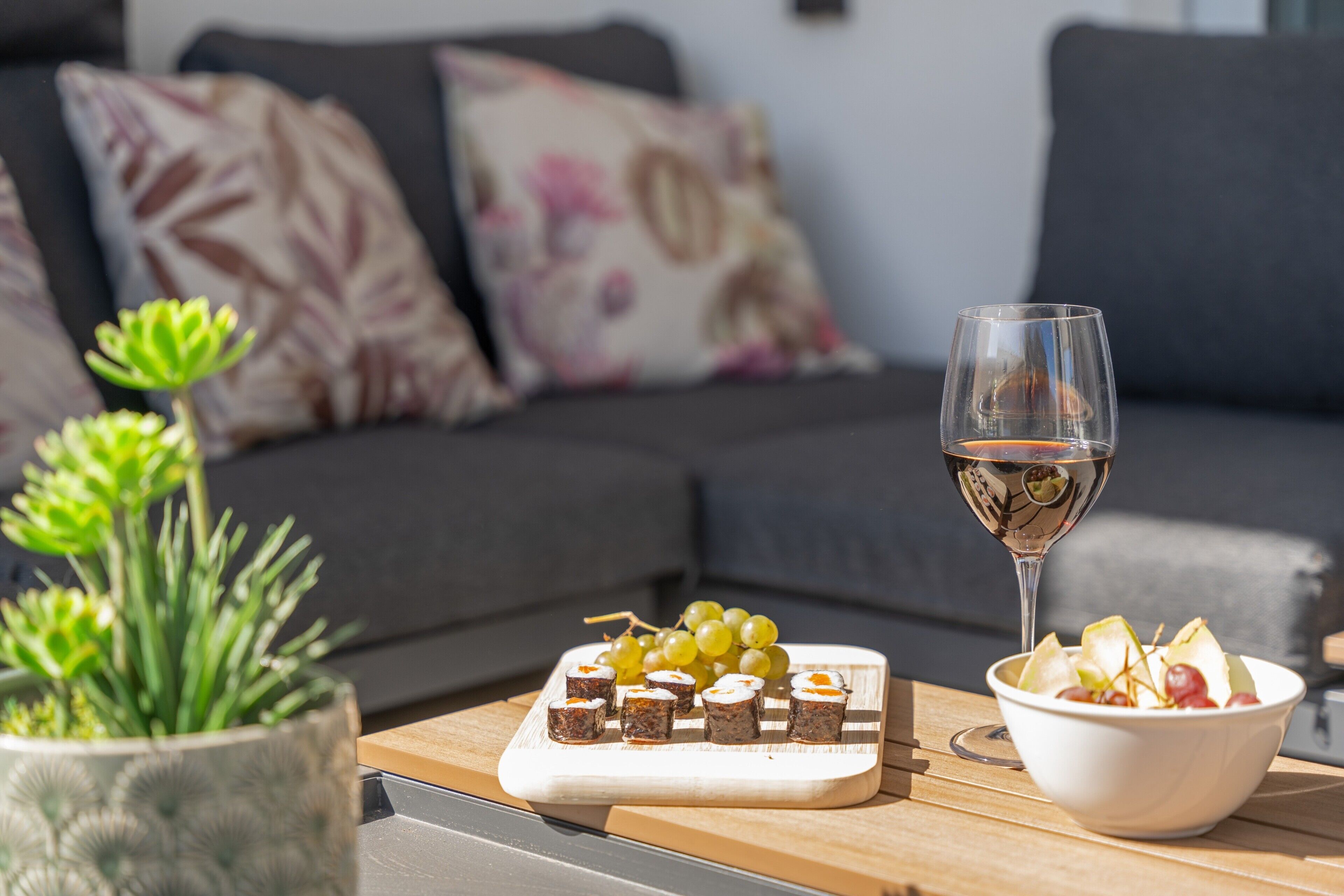 Una mesa de comedor con una bandeja de comida, una copa de vino y un bol de fruta.
