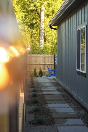 A pathway leading to a building with a wooden fence and a blue chair in the background. - New Cozy Modern Cottage with Hot Tub & Fire Pit! (Ponderay)