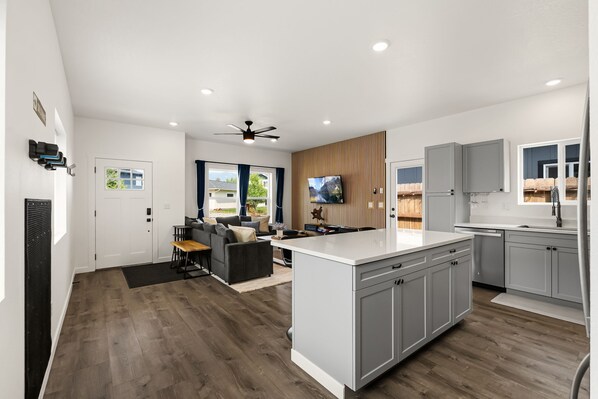 Cocina moderna con armarios grises, una isla central y un área de comedor con sofá y mesa de centro.